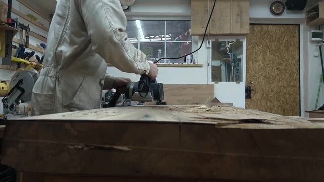 Low Angle Medium Shot of Professional Contractor Leveling Rough Lumber with Electric Planer in Workshop