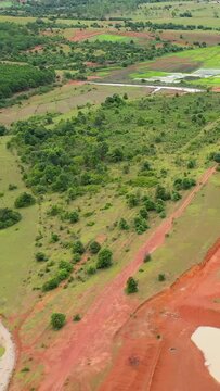 Aerial shot of the rural landscape in Plaine des Jarres, featuring green fields, scattered trees, and patches of red earth. Lush vegetation and agricultural plots are visible under natural daylight.