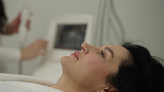 Relaxed middle-aged woman having modern anti-aging facial procedure, beautician applies microneedle rf device to skin for non-invasive lift and rejuvenation treatment, close-up, slow motion.