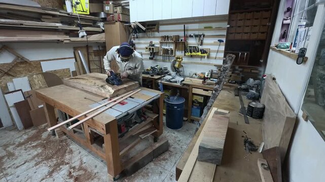 Woodworker in Full PPE Surfacing Timber Slab in Cluttered Workshop Wide Angle Establishing Shot