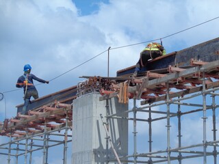 Two construction workers on metal scaffolding platform under bright daylight, focusing on safety gear and building progress – aerial perspective photo