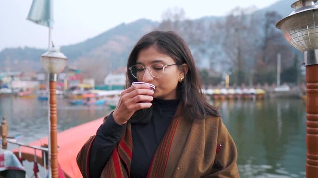 Portrait of Indian woman drink tea while standing at  house boat in Dal lake at Srinagar, Jammu and Kashmir, India. Tourist enjoying trip in mountains. Travel and holidays concept.