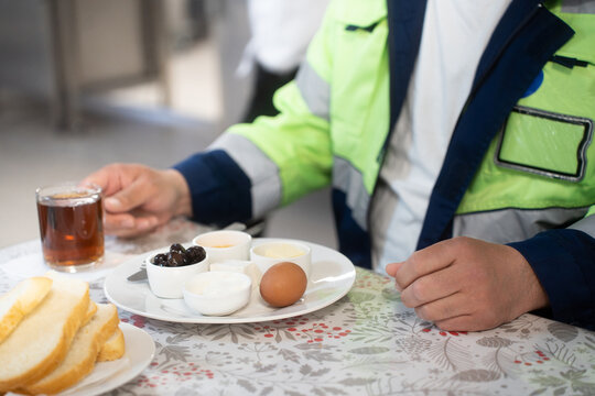 Industrial engineers sitting in canteen and talking on lunch break. Construction company workers in safety uniform eating meal and chatting in modern office