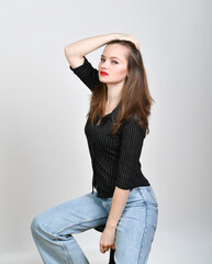Naklejka premium Selbstbewusstes Model posiert im Studio mit rotem Lippenstift und Jeans. Modernes Fashion-Porträt mit natürlichem Stil, Konzept für Mode, Lifestyle, Persönlichkeit und Stilbewusstsein.