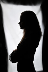 Naklejka premium Silhouette einer Frau im Gegenlicht mit verschränkten Armen. Künstlerisches Porträt mit klarer Kontur und dramatischem Licht, Konzept für Persönlichkeit, Stärke, Nachdenklichkeit und ästhetische Fotog