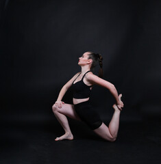 Obraz premium Sportliche Frau macht Dehnübung im Studio. Kombination aus Yoga, Pilates und Fitness-Training zur Entspannung, Beweglichkeit und Körperstärkung. Minimalistische Szene mit ruhigem Hintergrund.