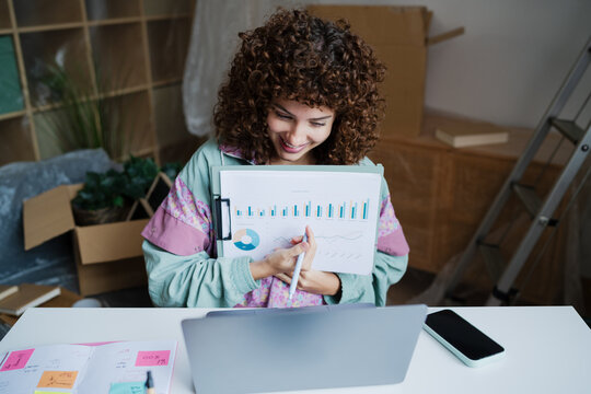 Smiling woman analyzing data at home workspace with laptop and charts