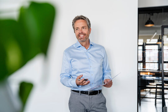 Smiling businessman in office holding document and smartphone
