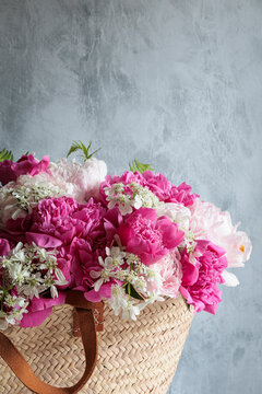 Studio floral arrangement of peonies and orlaya grandiflora in straw bag