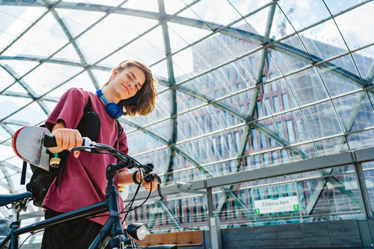 Modern teenager with skateboard and bicycle in urban glass station