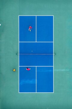 Aerial view of two players engaged in a vibrant pickleball match, the blue court a striking contrast against the green surroundings, Amelia Island, Florida, United States.