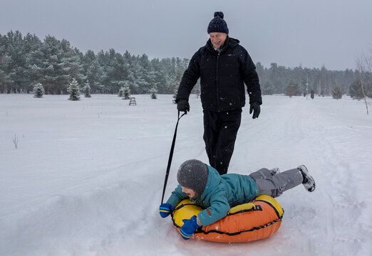 Elderly man pulling boy on inflatable circle outdoors in winter