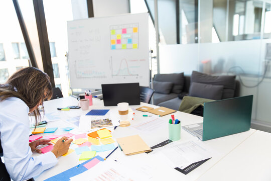 Woman writing sticky notes at planning workspace in modern office