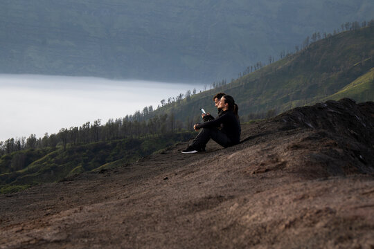 Couple sitting together at sunrise on Mount Bromo overlooking crater