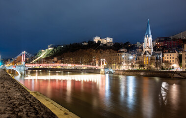 Fototapeta premium Lyon, france. December 29, 2023. Lyon cityscape at night showcasing the illuminated passerelle saint-georges and saint georges church reflecting in the calm saone river