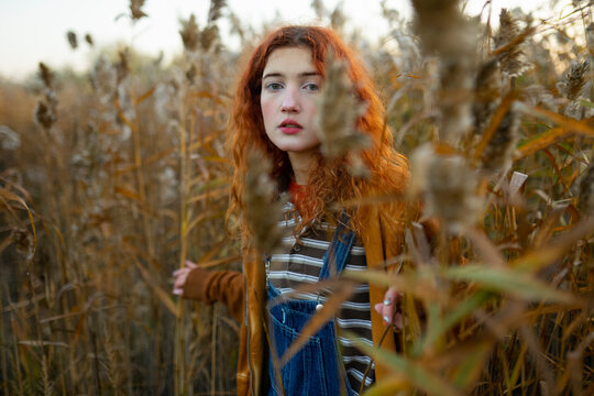 Red-haired woman in orange hoodie and denim overall in foggy reed forest