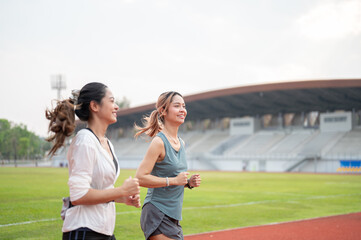 Obraz premium Side view athletic asian woman friend in sportswear running jogging together on racetrack in stadium
