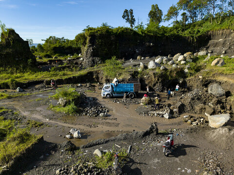 Aerial view of a dusty quarry where workers and a truck stand amid piles of rocks and earth, Woro River, Klaten Regency, Central Java, Indonesia.