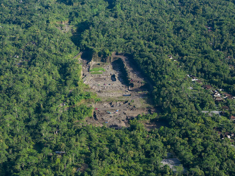 Aerial view of a dramatic scar on the lush landscape near the Woro River, where earth tones clash with vibrant greenery, Klaten Regency, Central Java, Indonesia.