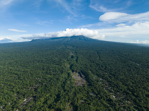 Aerial view of lush forest blanketing the landscape, stretching towards a majestic mountain peak veiled in soft clouds, Woro River, Klaten Regency, Central Java, Indonesia.