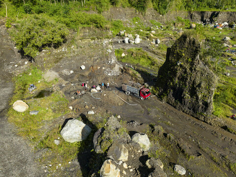Aerial view of a red truck amidst the dark earth, contrasting with the vibrant green foliage on the river banks, Woro River, Klaten Regency, Central Java, Indonesia.