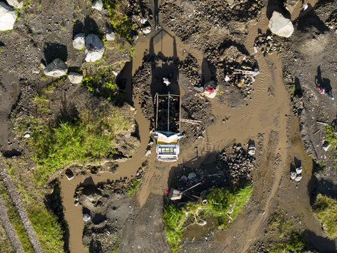 Aerial view of a truck wading through the muddy Woro River, its white and blue paint contrasting with the dark earth, Klaten Regency, Central Java, Indonesia.