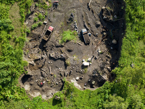 Aerial view of trucks scattered across a construction site, amidst the stark contrast of dark earth and vibrant green vegetation, Klaten Regency, Central Java, Indonesia.