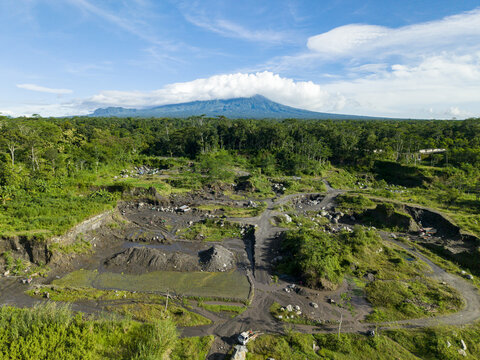 Aerial view of the stark, dark earth contrasting with the vibrant green vegetation, with a mountain backdrop under a bright sky, Klaten Regency, Central Java, Indonesia.