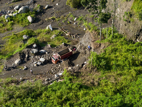 Aerial view of a truck amidst the rugged terrain of Woro River, where dark soil meets verdant foliage, Klaten Regency, Central Java, Indonesia.