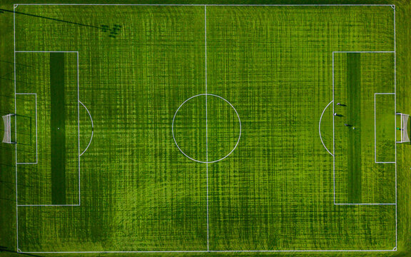Aerial view of a lush green soccer field, its white lines sharply contrasting against the verdant grass, casting long shadows under the open sky, Warsaw, Masovian Voivodeship, Poland.