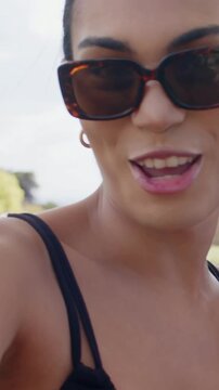 Vertical video: Smiling woman tortoise sunglasses laughing with pal as camera pulling back at park
