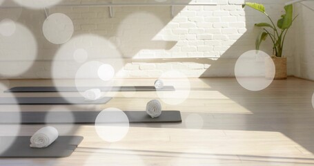 Lining dark gray yoga mats with rolled white towels on wooden floor in sunlit studio