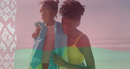 Naklejka premium Wrapping mother in yellow tank draping turquoise-striped towel around daughter on sand, panel left