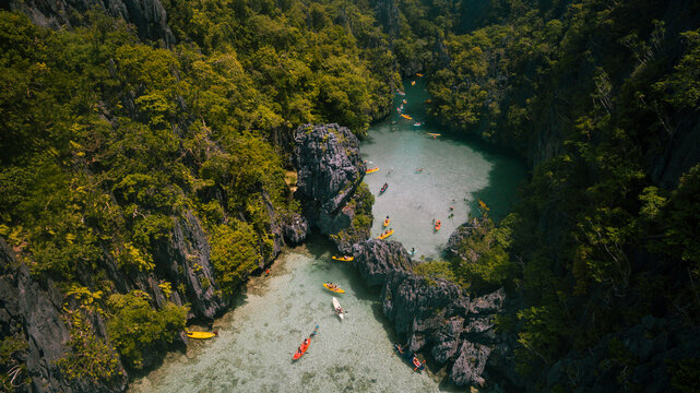 Aerial view of boats dotting the turquoise waters near towering limestone cliffs shrouded in emerald foliage, El Nido, Mimaropa, Philippines.