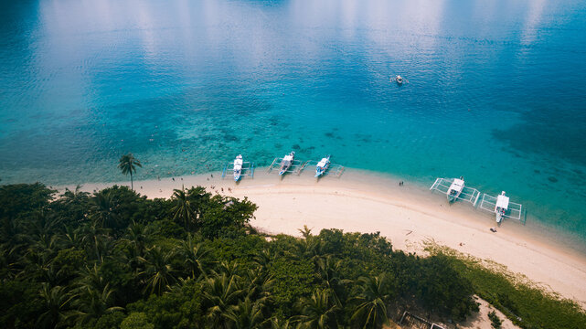 Aerial view of boats resting on the shore of a pristine beach, where turquoise waters meet lush green forests, creating a vibrant contrast, El Nido, Mimaropa, Philippines.