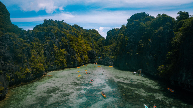 Aerial view of kayaks dotting the turquoise waters nestled amidst jagged cliffs cloaked in verdant foliage, El Nido, Mimaropa, Philippines.