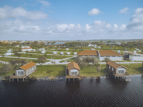 Aerial view of stilt houses lining the tranquil lagoon's edge with a vibrant campsite nestled in the background, Praia de Mira, Coimbra, Portugal.