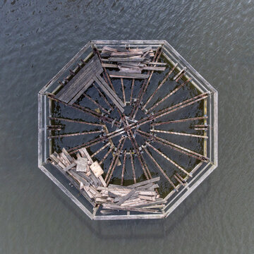 Aerial view of the octagonal structure with decaying wooden beams and debris amidst the still waters of Beatrixpark, Almere, Flevoland, Netherlands.