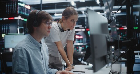 Fototapeta premium Female Manager Advising Young Male Trader in Busy Financial Office. Analyst With Supervisor Review Complex Analytics on Display, Gesturing Towards Key Data Points. Mentorship and Office Coordination.