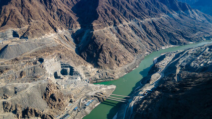 Aerial view of mountain river dam construction site in rugged canyon landscape. © Yanyong