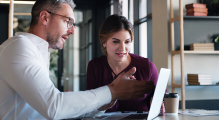 Creative, woman and man with advice on laptop for editorial guidance, story review or feedback. Journalist, lead editor or meeting with tech in newsroom for fact checking, headline idea or teamwork