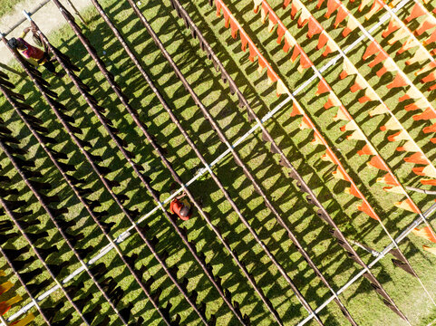 Aerial view of vibrant orange and yellow triangular flags casting linear shadows across the lush green field, creating a geometric dance of light and shade, Narayanganj, Bangladesh.