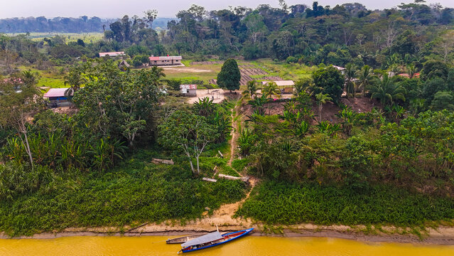 Aerial view of the riverbank homes nestled amidst the deep green jungle foliage, kissed by the golden river, Puerto Maldonado, Madre de Dios, Peru.
