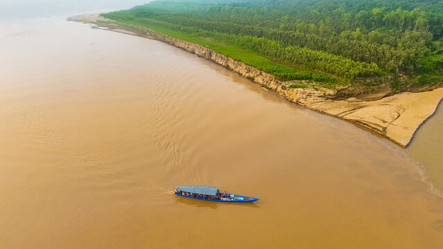 Aerial view of a boat navigating the muddy river against the backdrop of lush green forest, Puerto Maldonado, Madre de Dios, Peru.
