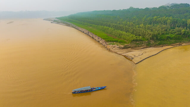 Aerial view of the confluence of muddy rivers flowing into each other, split by a strip of green forest, with a boat sailing in the murky water, Puerto Maldonado, Madre de Dios, Peru.