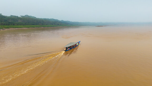 Aerial view of a boat cutting through the muddy waters of the river under a misty sky, Puerto Maldonado, Madre de Dios, Peru.