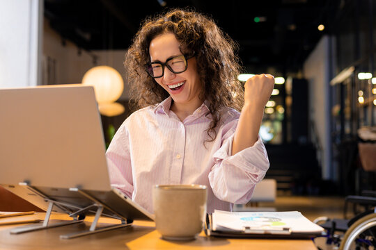 Happy woman winning with laptop raising hand posing in coworking office