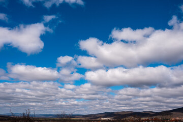 Wide panoramic view of a bright blue sky filled with fluffy white cumulus clouds over a distant mountain horizon.