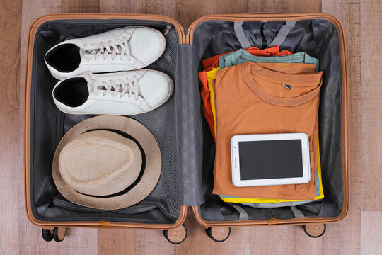 Packed Travel Bag Ready For Departure, Featuring Summer Accessories And Tablet On Wooden Surface