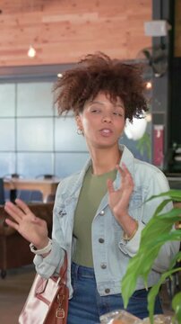 Vertical video: Reacting to offscreen voice, two women talking at cafe counter, jacket, plant, bag